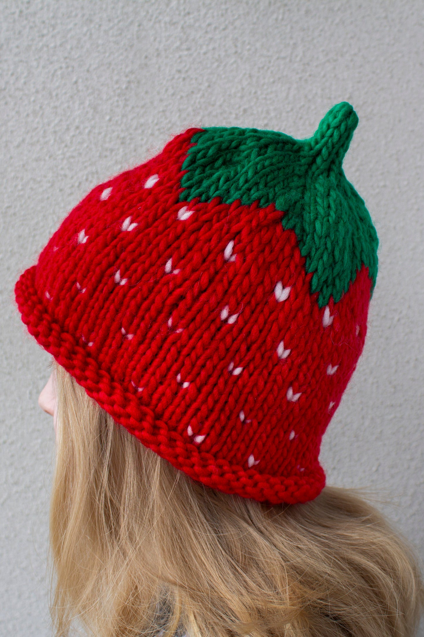 Muhkea, pehmeä ja lämmin punainen mansikkapipo vaaleahiuksisen aikuisen naisen päässä.