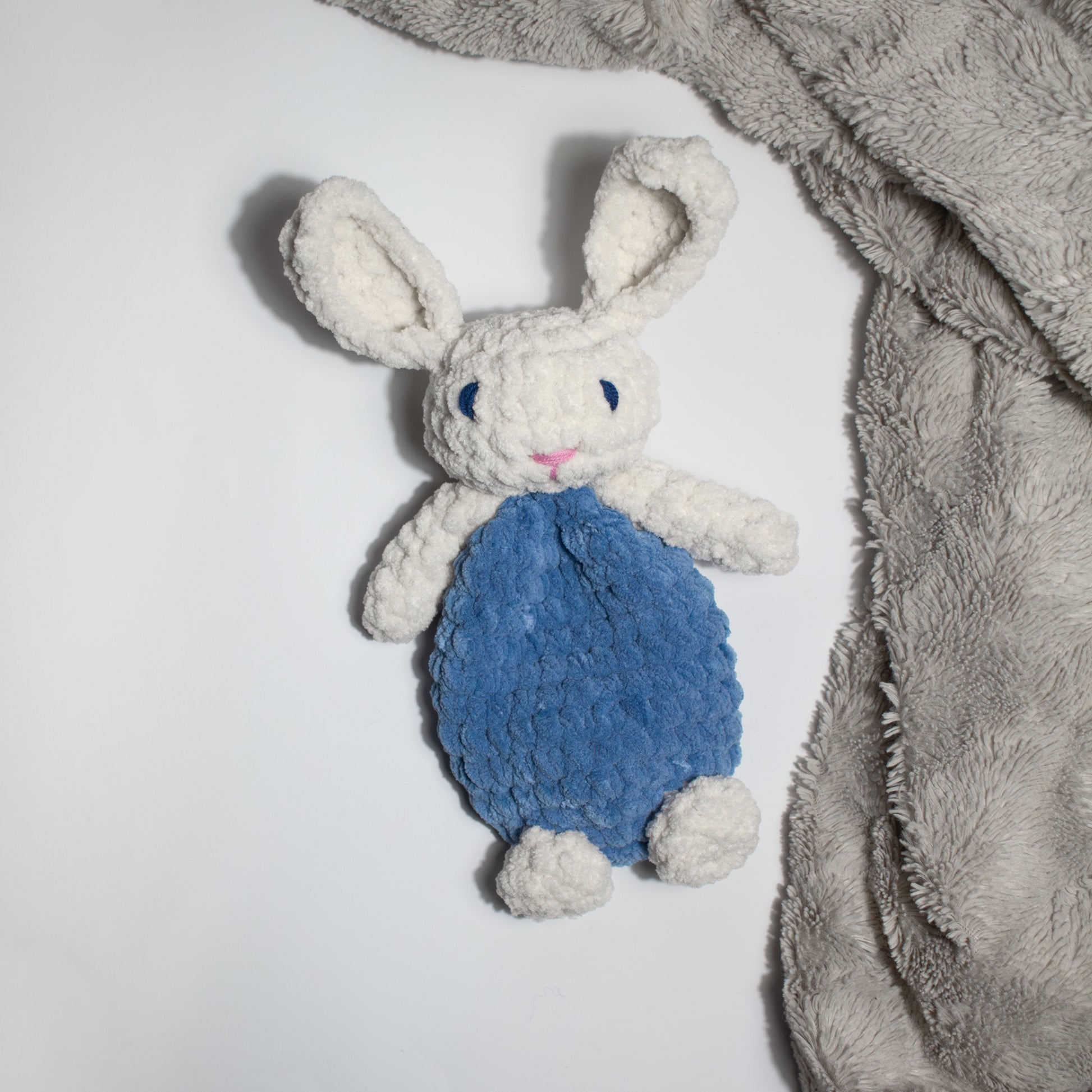 Sininen käsintehty söpö unipupu vauvalle ensileluksi, joka pöydällä pehmeän beigen viltin vieressä.