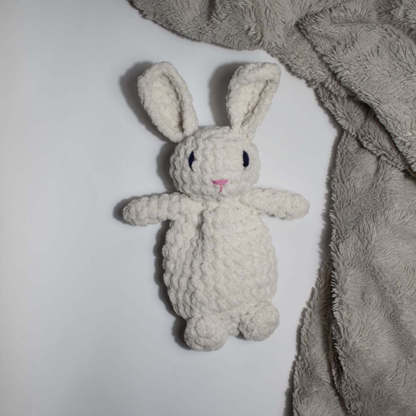 Valkoinen käsintehty söpö unipupu vauvalle ensileluksi, joka pöydällä beigen viltin vieressä.