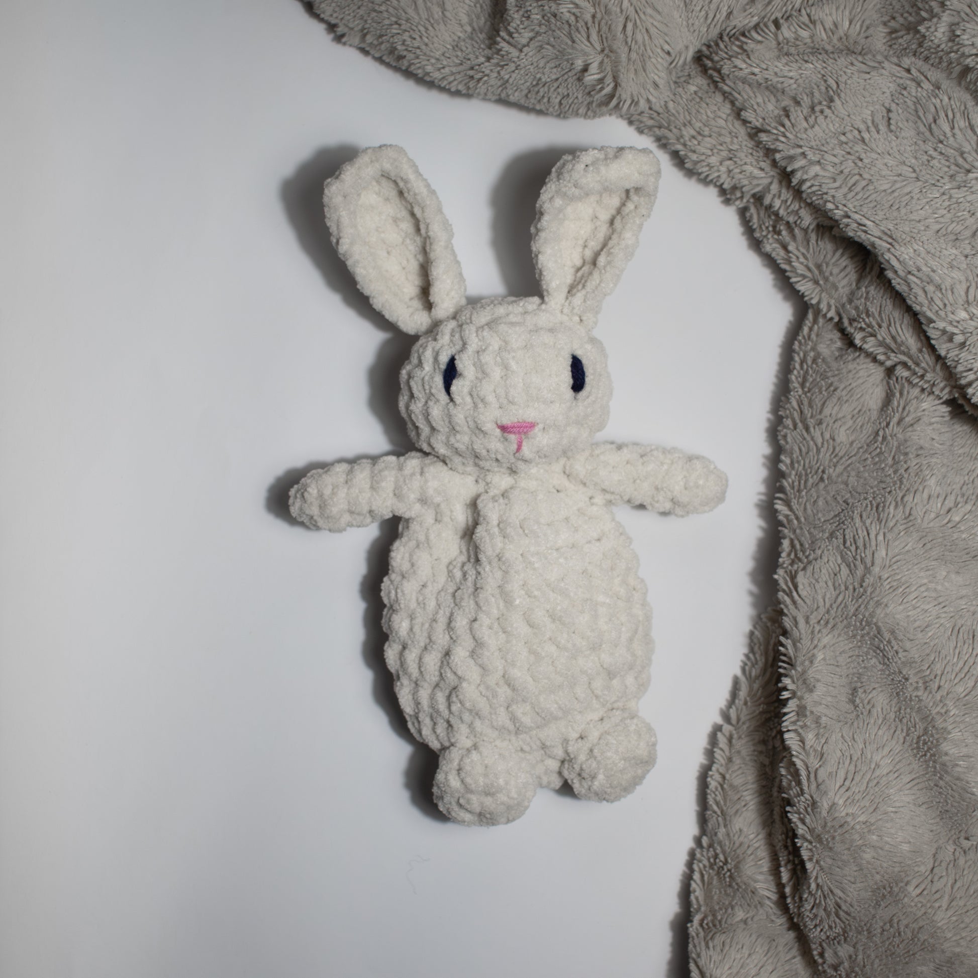 Valkoinen käsintehty söpö unipupu vauvalle ensileluksi, joka pöydällä beigen viltin vieressä.