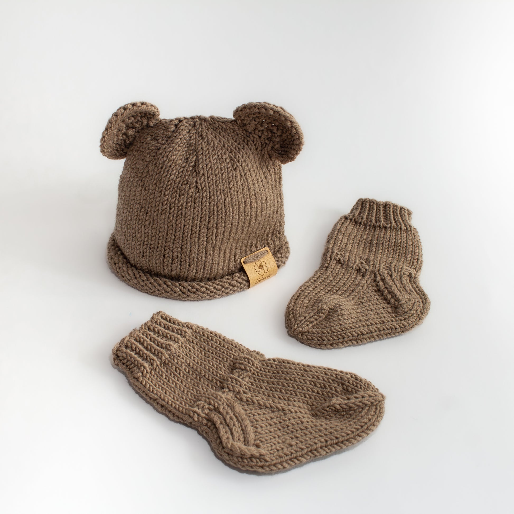 Ruskea käsintehty neulottu nallepipo jossa korvat sekä kaksi pientä vauvan ruskeaa nalle villa sukkaa.